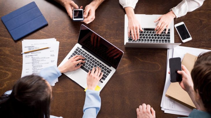 Overhead view of young businesspeople sitting together at workplace and using digital devices